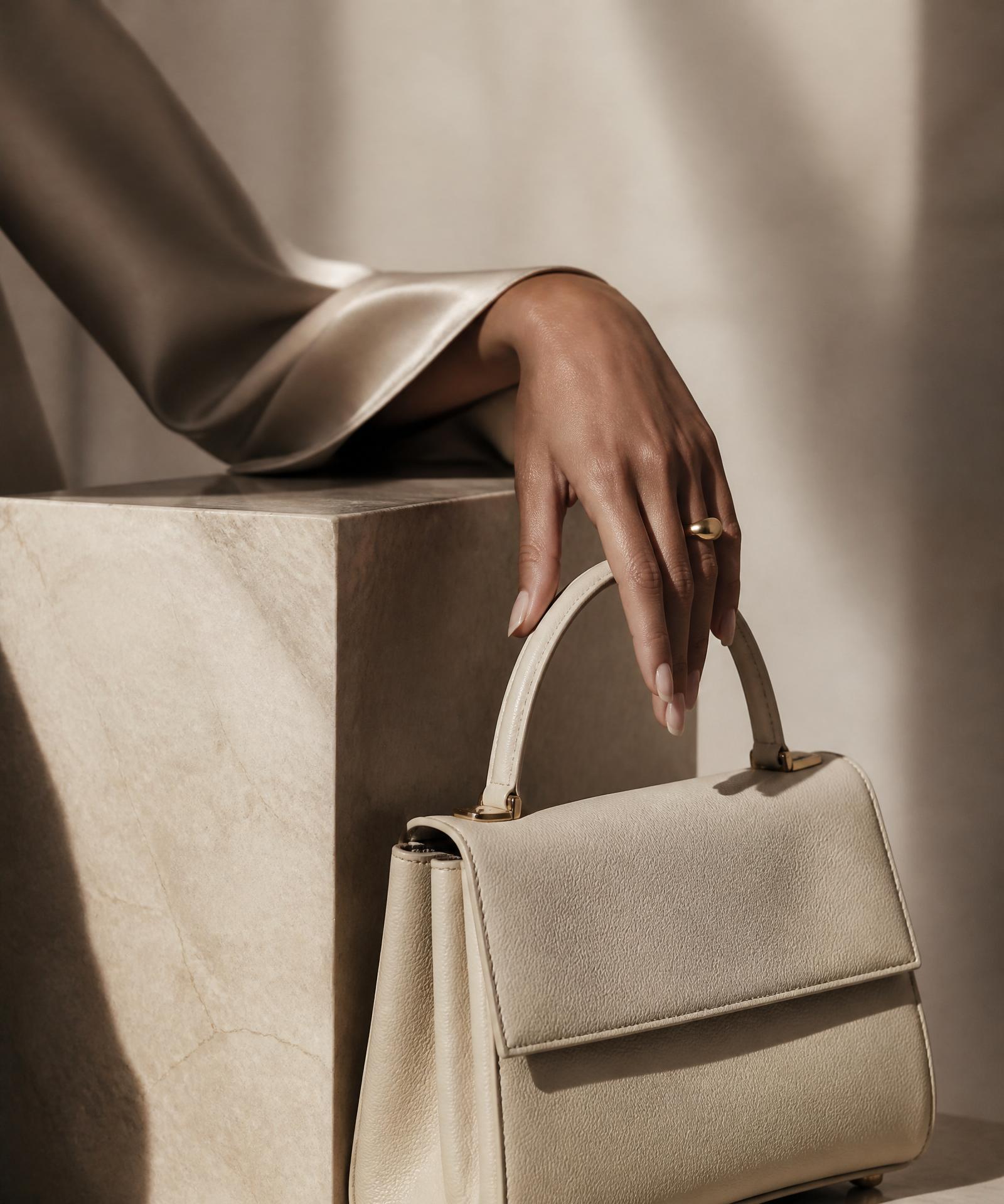 A Leoprè ivory leather handbag held against soft champagne silk